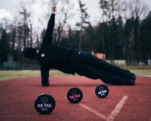 Plank vedle tří KB TAGů na atletické dráze